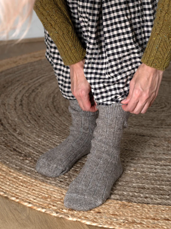 Person wearing gray socks and a checkered dress on a woven surface