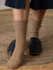 Person wearing brown socks and black shoes on a textured surface