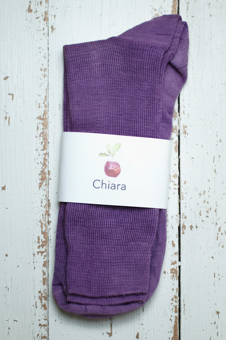 Purple socks with a 'Chiara' label on a white wooden surface