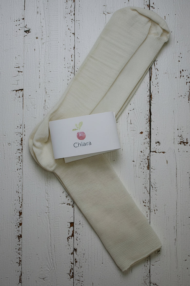 Off white wool socks with a 'Chiara' branded label on a light wooden floor.