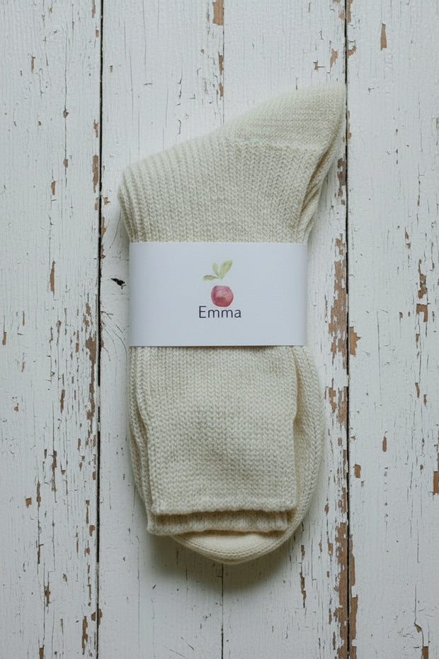 White wool sock on white timber floor background with a white label showing a red apple and Emma written underneath