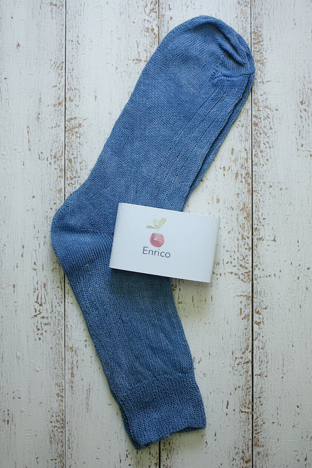 Blue sock on a wooden surface with a white card displaying 'Enrico' branding.