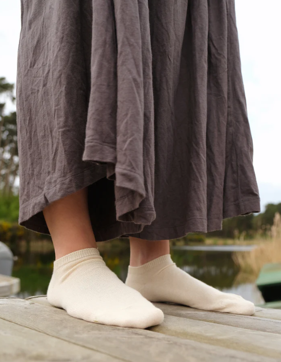 Person wearing white socks and a brown skirt standing on a wooden dock with a natural background.