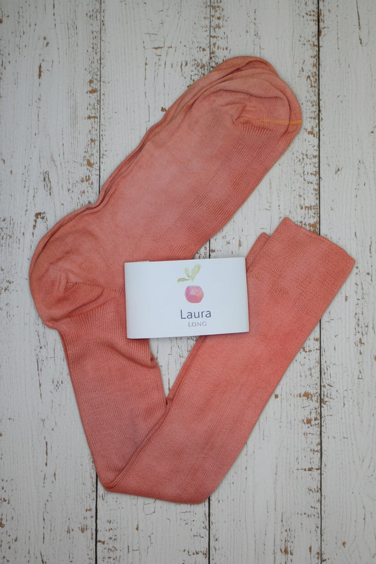 Pair of pink long socks with a 'Laura' brand card on a wooden surface