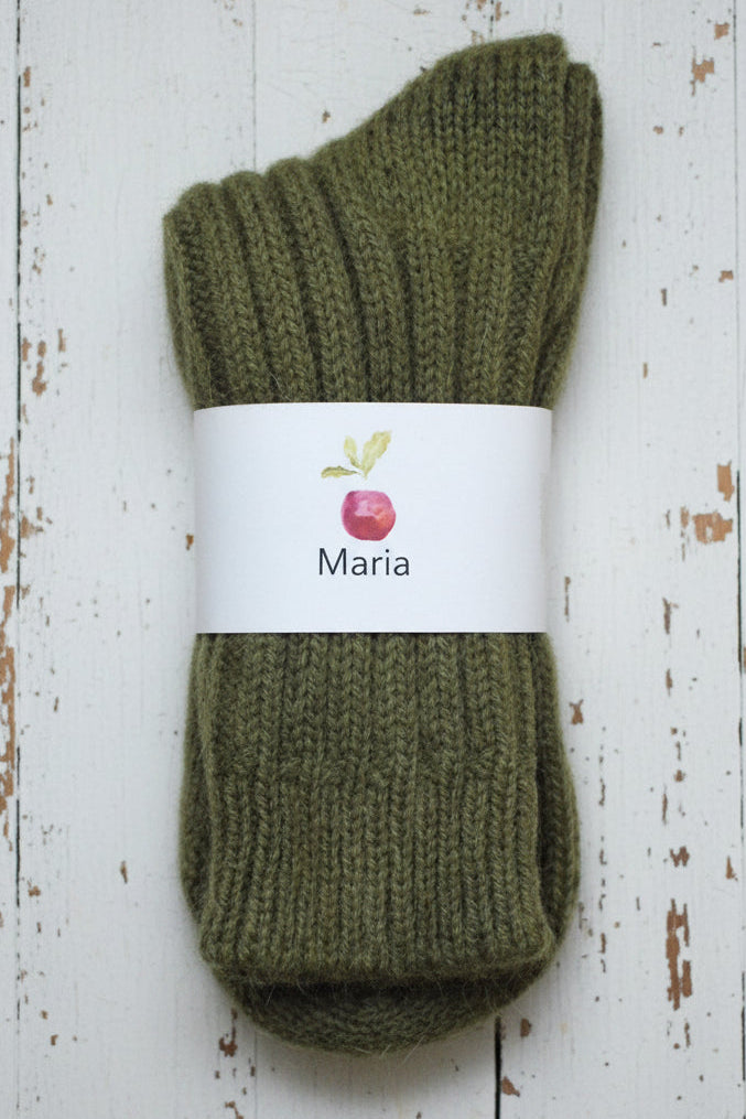 Pair of green knitted socks with a 'Maria' label on a white wooden surface