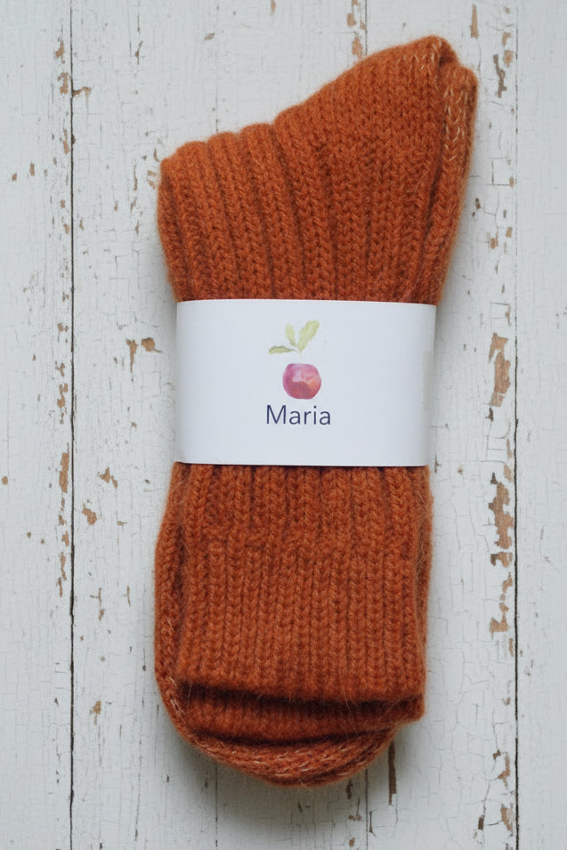 Pair of orange socks with a 'Maria' label on a white wooden surface