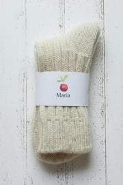 A pair of white woolly socks on a white background with a white label showing a red apple and MAria in black ink