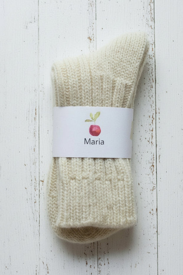 A pair of white woolly socks on a white background with a white label showing a red apple and MAria in black ink