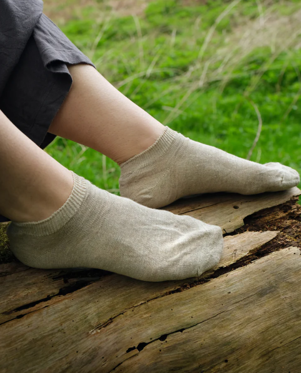 Person wearing beige socks sitting on a log with grass in the background