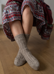 a person sitting cross legged with beige wool socks and wearing a colour skirt