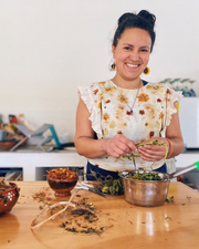 Woman in a kitchen preparing natural dyes with various ingredients on a table.