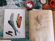 Artistic drawings of leaves on a piece of paper next to a sketchbook with notes on a textured surface.