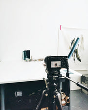 Camera on a tripod with a white wall and art in the background