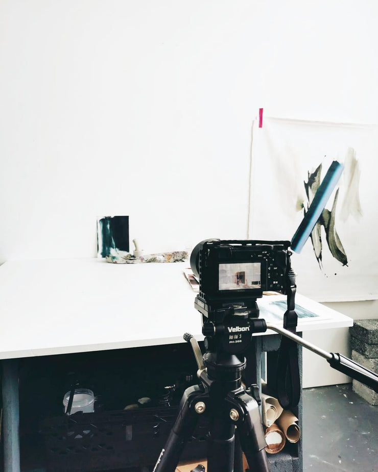 Camera on a tripod with a white wall and art in the background