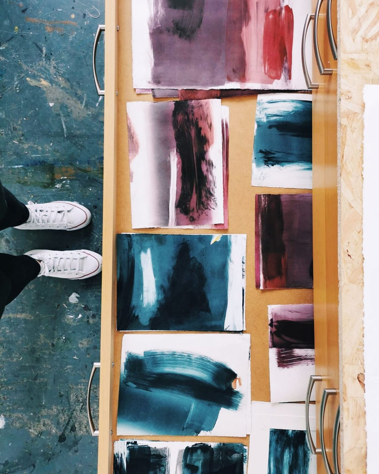 Artistic abstract paintings on a wooden ladder against a textured wall.