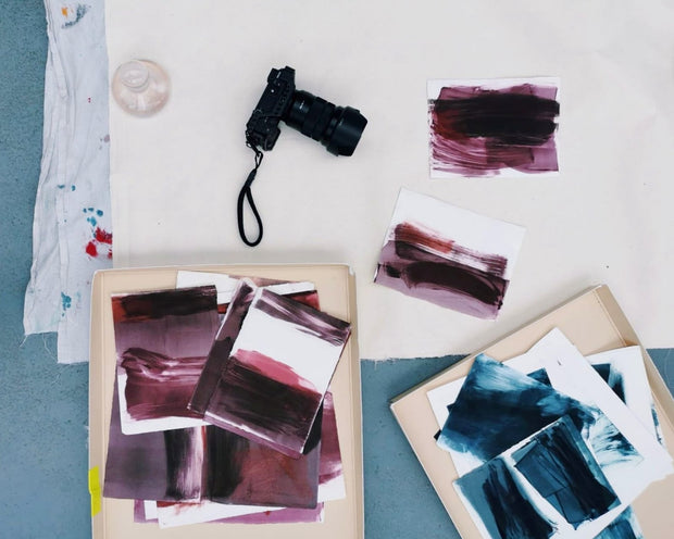 Artistic swatches of paint on paper with a camera on a light surface.