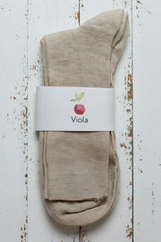 Beige sock on white timber background with a white label showing an apple and viola written on it.
