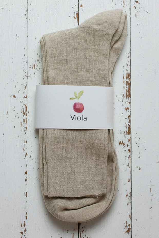 Beige sock on white timber background with a white label showing an apple and viola written on it.