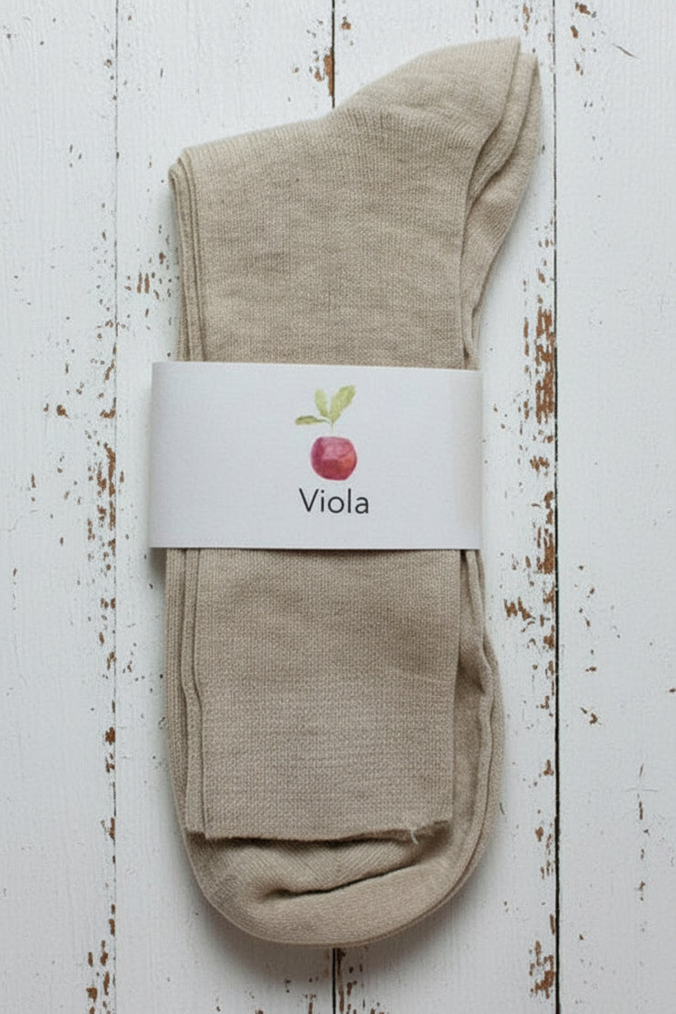 Beige sock on white timber background with a white label showing an apple and viola written on it.