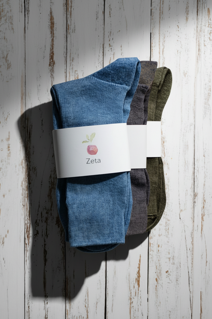 Three pairs of socks, one blue, one purple and one brown, with a Zeta label on a wooden surface.