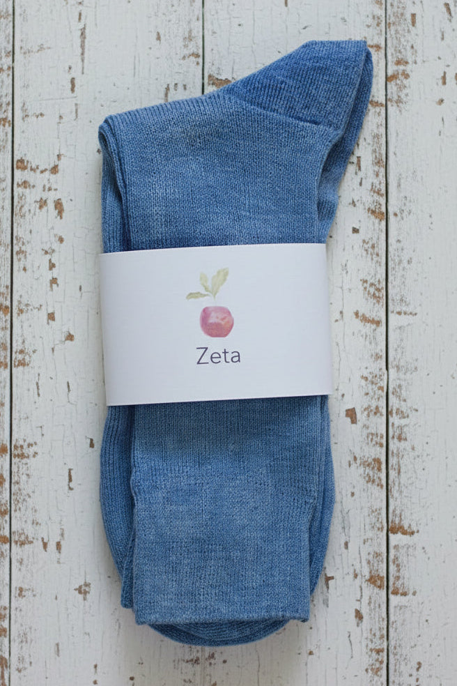 Pair of blue linen socks with a 'Zeta' label on a wooden surface