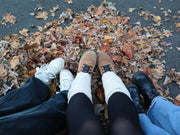 3 pairs of legs and shoes on a pile of autumn leaves