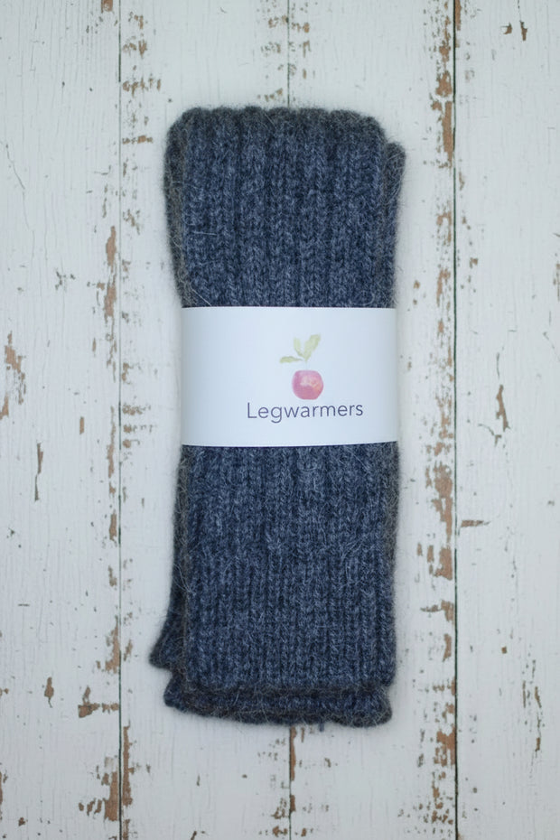 Pair of dark grey knitted legwarmers on a white wooden surface with a label.