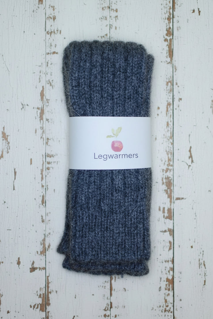 Pair of dark grey knitted legwarmers on a white wooden surface with a label.
