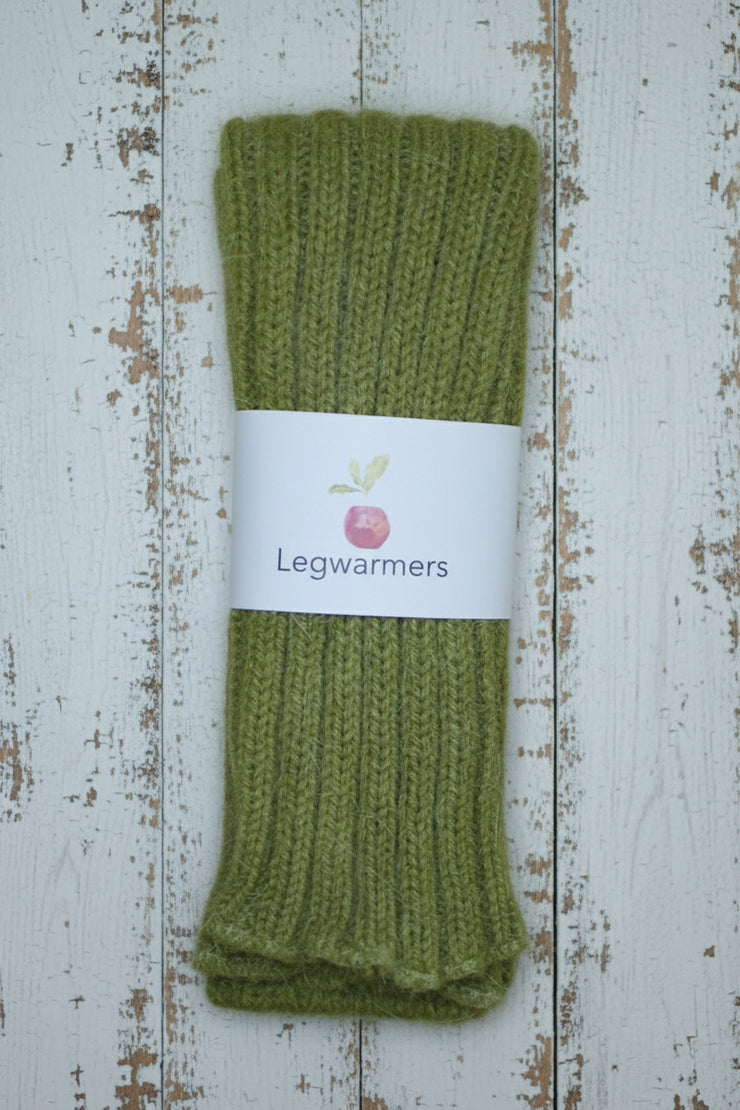 Green knitted legwarmers with a white label on a white wooden surface