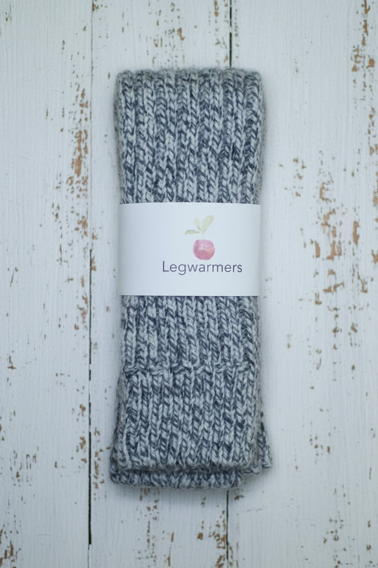 Grey knitted legwarmers with a label on a wooden surface