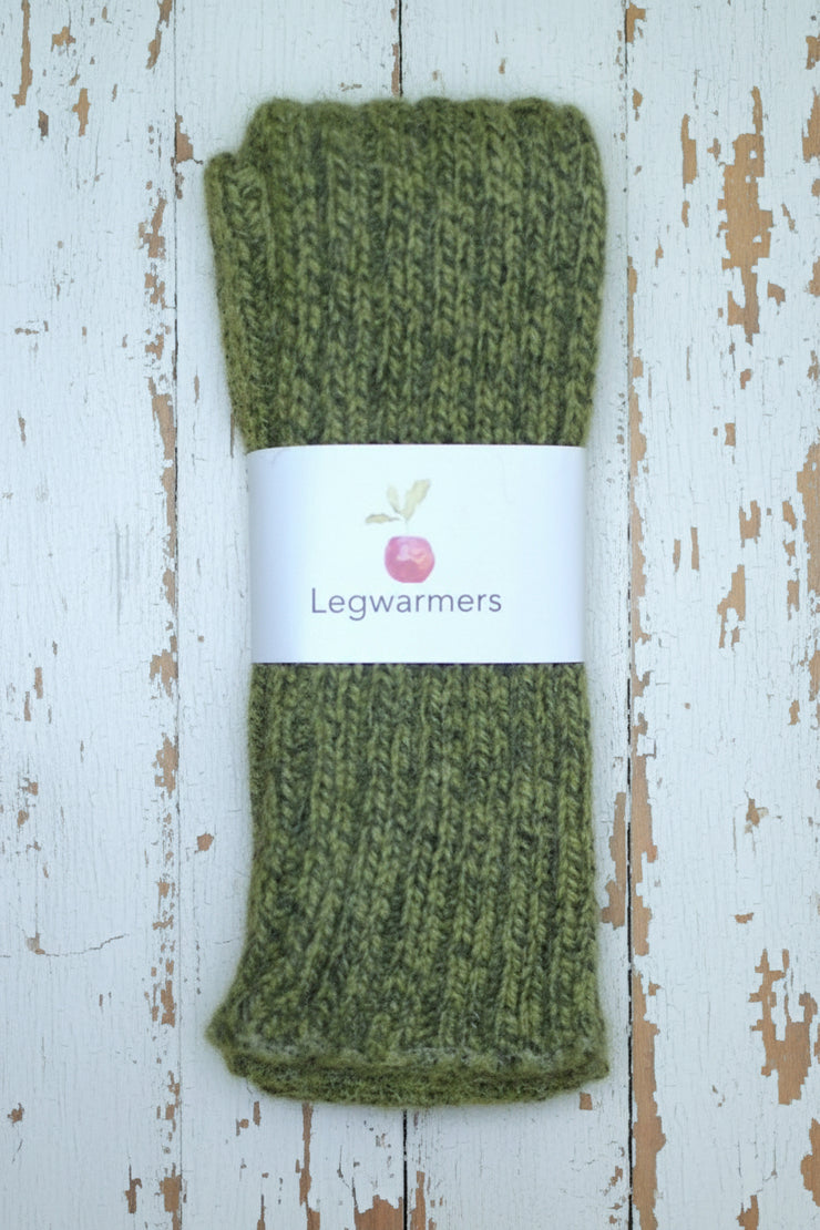 Mottled Green knitted legwarmers with a label on a white wooden surface