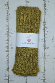 Pair of mustard yellow knitted legwarmers on a rustic wooden surface with a label.