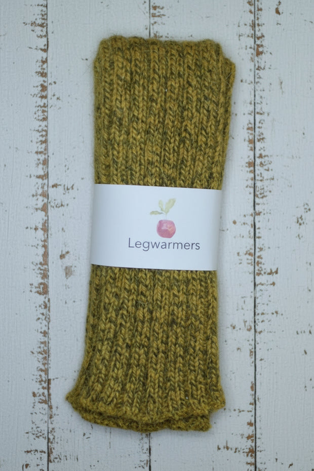 Pair of mustard yellow knitted legwarmers on a rustic wooden surface with a label.