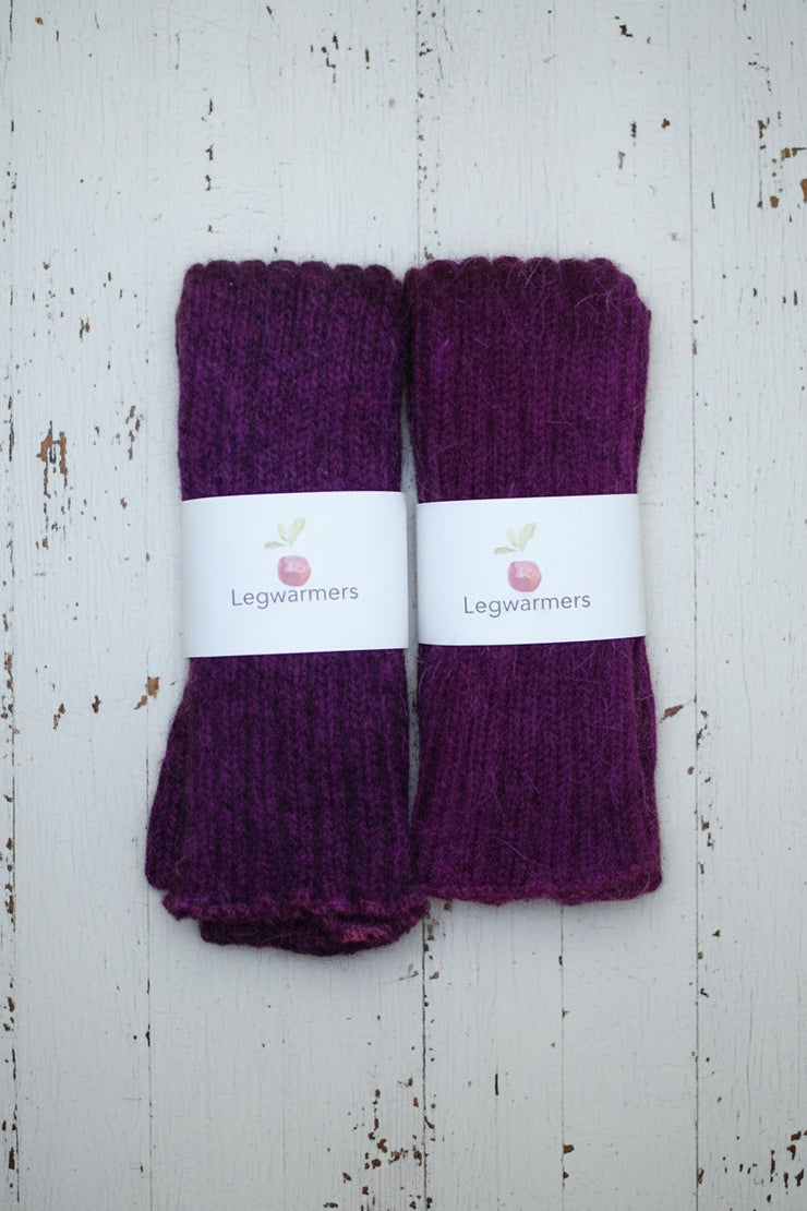 Two pairs of purple legwarmers on a white wooden surface with visible brand labels.
