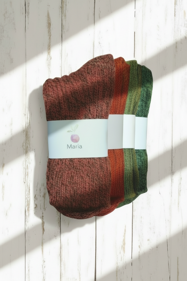 A pile of different coloured Maria wool  socks with a visible brand label on a white wooden surface, with a window shadow falling across it.