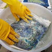 Person wearing yellow gloves cleaning a piece of artwork in a white bowl.