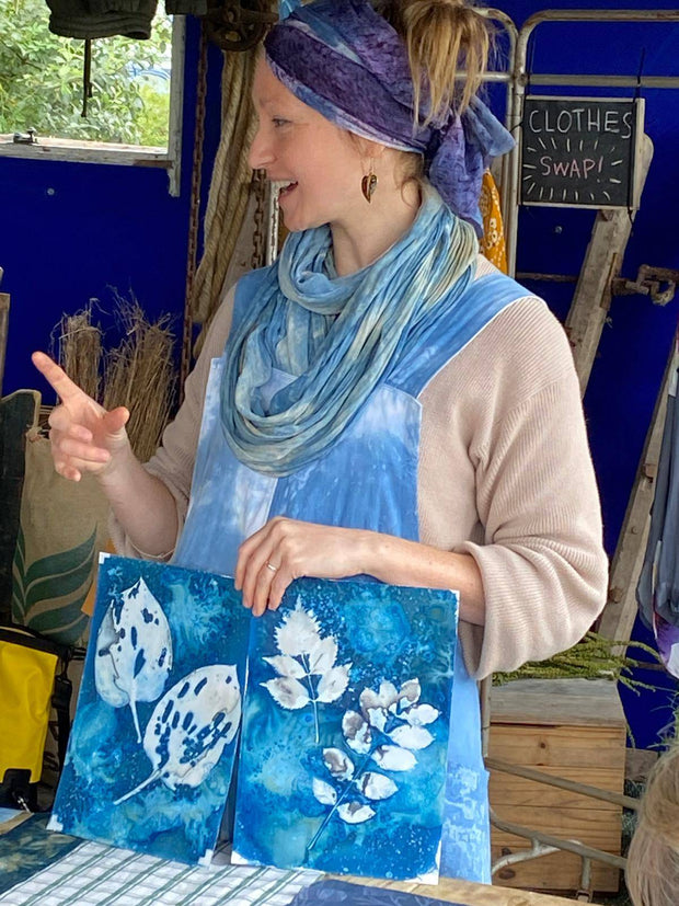 Woman holding two blue artworks with white leaf designs at an outdoor event.